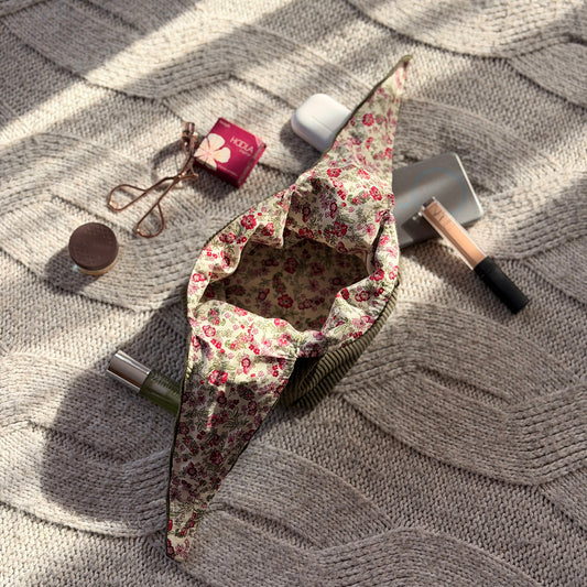 An empty styled flat-lay olive green corduroy make up organiser bag with a pink ditsy floral lining with beauty products scattered around. Cottagecore aesthetic. Surrounded by beauty products