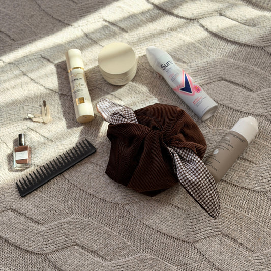 A styled flat-lay chocolate brown corduroy make up beauty organiser bag with a dark brown gingham lining with beauty products scattered around. Poetcore aesthetic. 