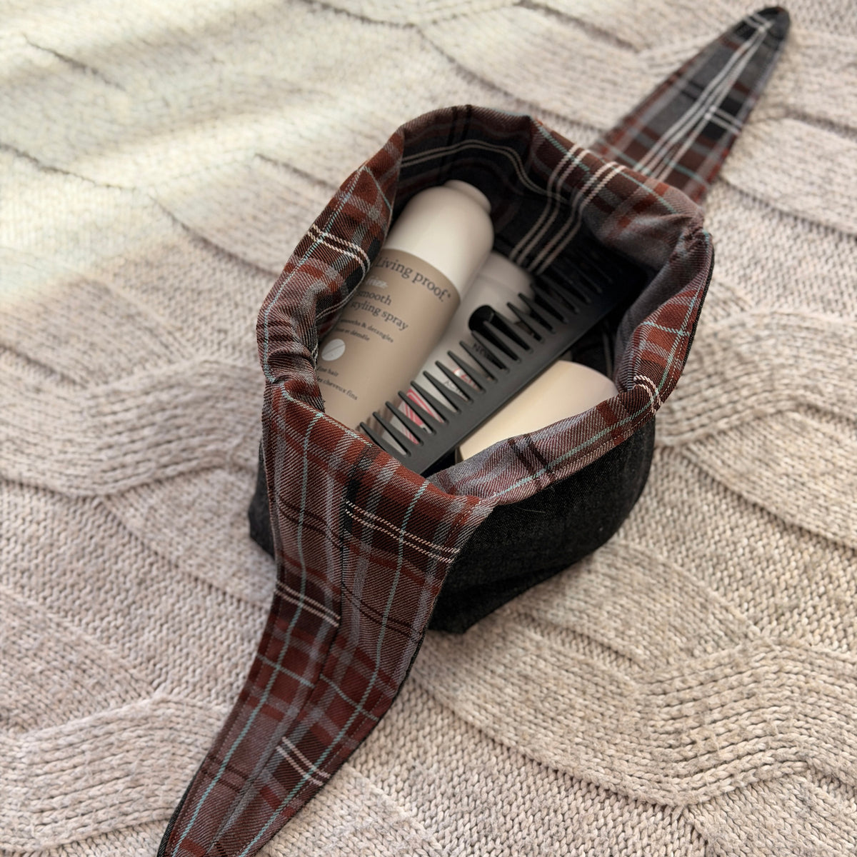 A filled styled flat-lay black denim make up beauty bag with a brown and grey tartan lining with beauty products scattered around. Dark Academia aesthetic. Filled with beauty products.
