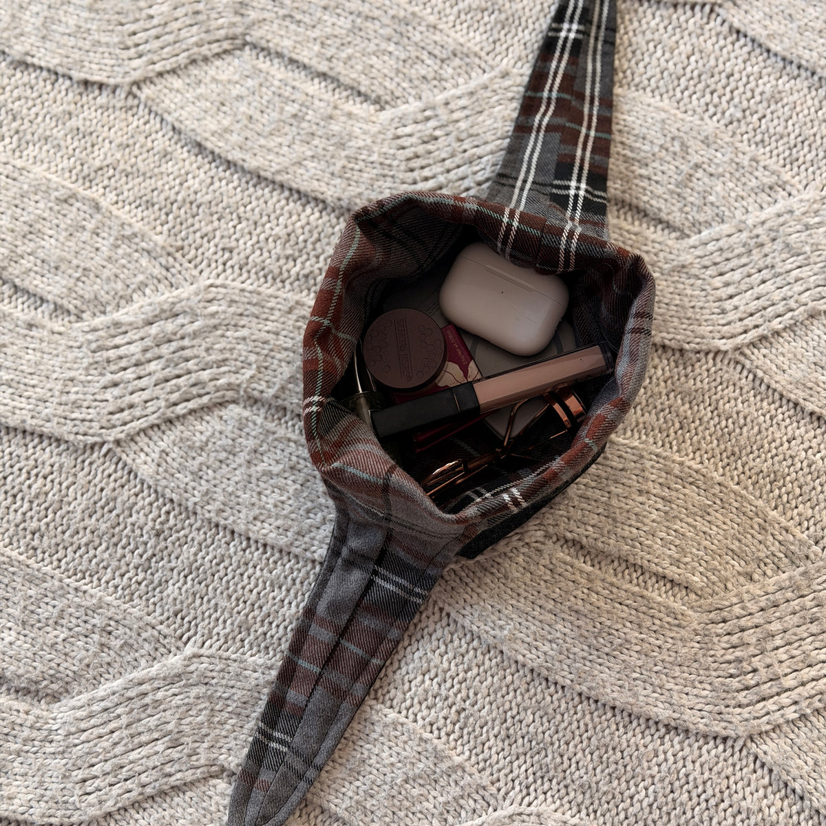 A styled flat-lay black denim make up organiser bag with a brown and grey tartan lining filled with with beauty products. Dark Academia aesthetic. Surrounded by beauty products.