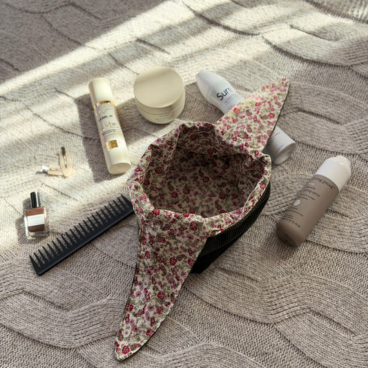A styled flat-lay empty olive green corduroy make up beauty bag with a pink ditsy floral lining with beauty products scattered around. Cottagecore aesthetic. Surrounded by beauty products.