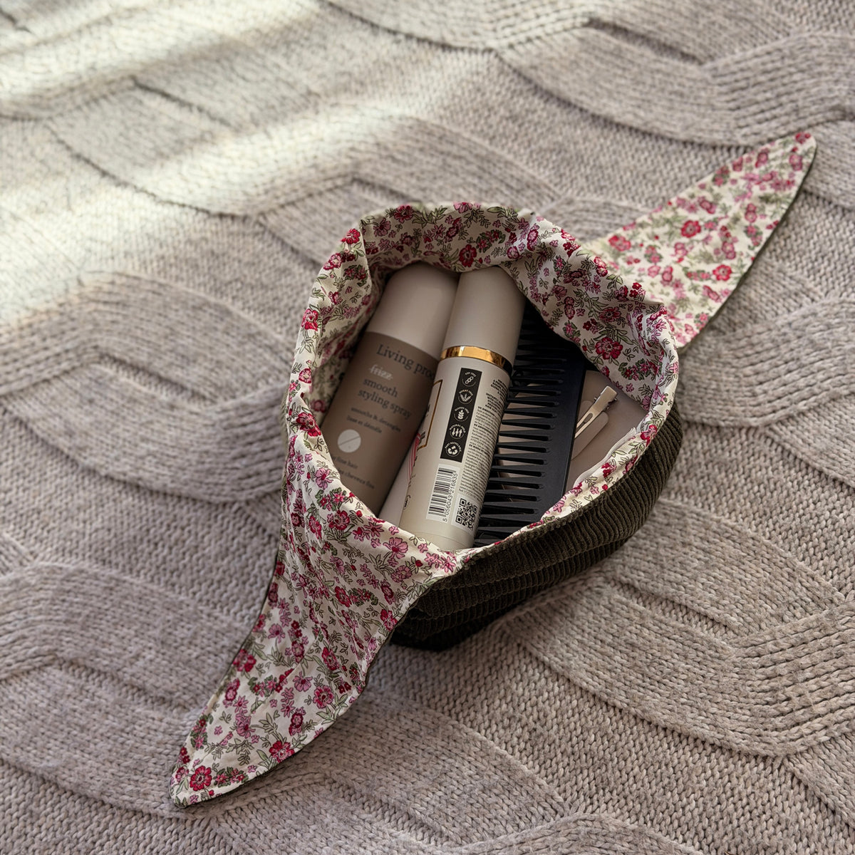 A styled flat-lay filled olive green corduroy make up beauty bag with a pink ditsy floral lining with beauty products. Cottagecore aesthetic. 