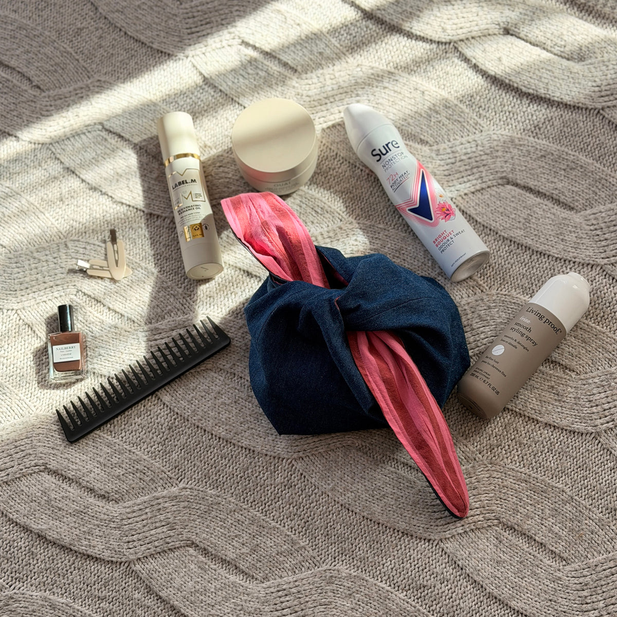 A styled flat-lay dark denim make up beauty bag with striped pink and maroon lining with beauty products scattered around. Y2k aesthetic