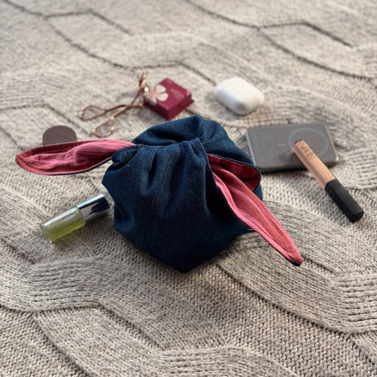 A styled flat-lay dark denim organiser bag with striped pink and maroon lining with beauty products scattered around. Y2K aesthetic.