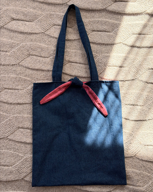 A dark denim blue fabric tote bag with long shoulder straps with pink and maroon striped lining.  Y2K aesthetic.