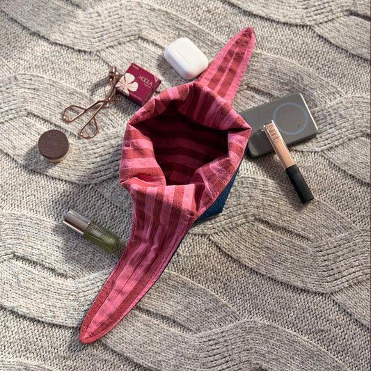 A styled flat-lay dark denim organiser bag with striped pink and maroon lining with beauty products scattered around. Y2K aesthetic.